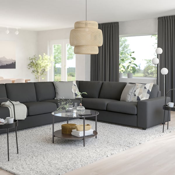 Minimalistiskt vardagsrum med grå VIMLE soffa, soffbord i glas, inredning, pendellampa, svarta gardiner, golvlampa, lugn utomhusutsikt.