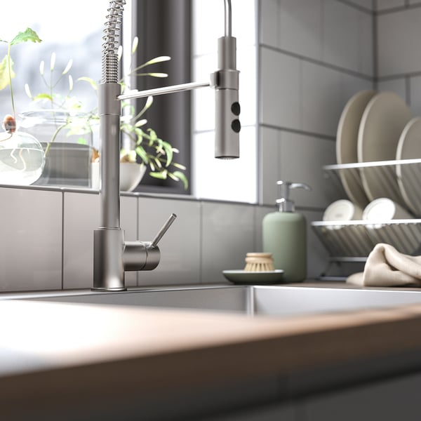 Modern köksblandare, VIMMERN i rostfritt stål. Elegant design med flexibel handspray. Hög, smal form, omgiven av tallrikar och tvålpump.