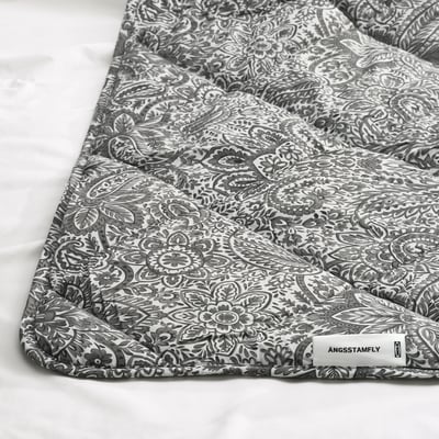 Grey and white patterned duvet partially folded, showcasing intricate flower design. White tag labelled ÄNGSSTAMFLY visible.