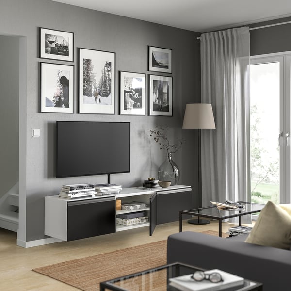 Modern living room with BESTÅ tv stand, flat screen tv, couch, coffee table, and floor lamp. Black and white framed photos on dark grey wall.