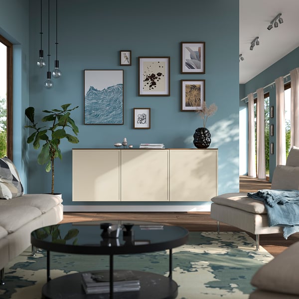 Modern living room with teal walls, BESTÅ sideboard, art, and black coffee table in front of grey sofa. Large window with curtains and matching rug.