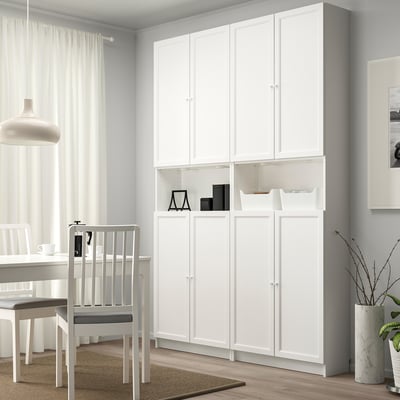 White BILLY bookcase with panel doors, tall, between table and window, ample storage.