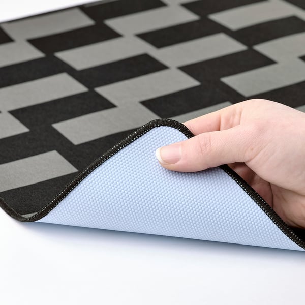Person holding a grey and black chequered gaming mouse pad, showing its textured back.