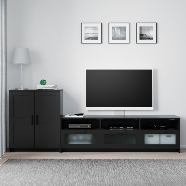 Modern minimalist living room with black BRIMNES tv stand, large flat-screen tv, cabinets, lamp, books, and art frames.