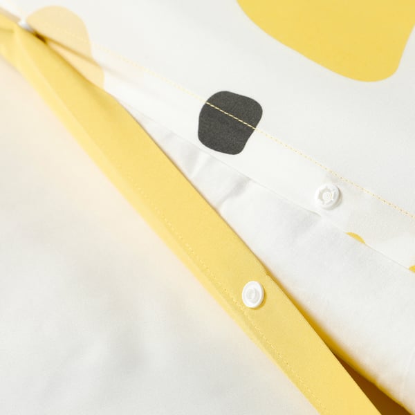 Close-up of bedlinen with yellow trim and black patch. Button detail shown.