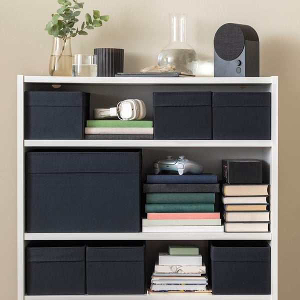 Bookshelf with black fabric storage boxes, books, headphones, and decorative items.