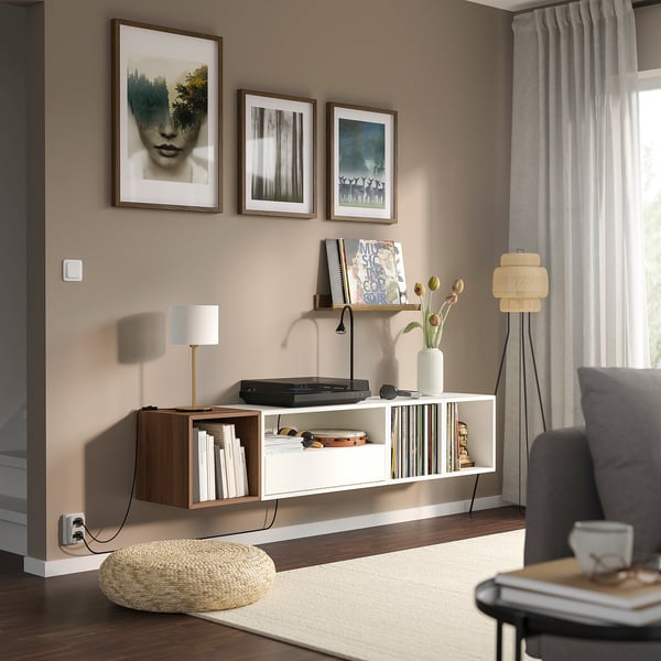 Modern living room with EKET shelves, books, records, and a lamp. Grey armchair, beige rug, and natural-contemporary style.