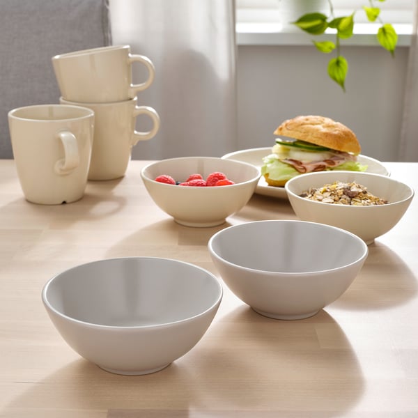 Four white bowls and stacked cups on a table with food. Ideal for simple, versatile dining.