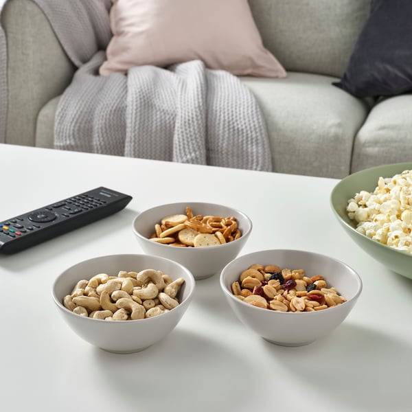 Four bowls of snacks and a tv remote on a coffee table.