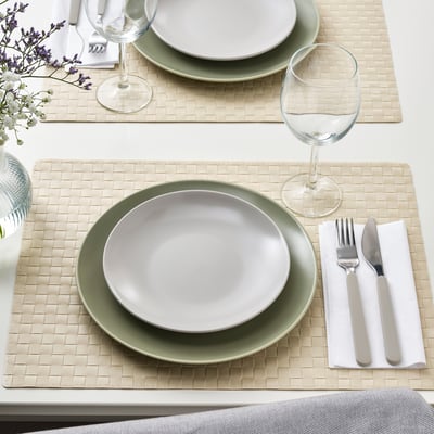Two places settings with green and white plates, glassware, cutlery, and woven placemats.
