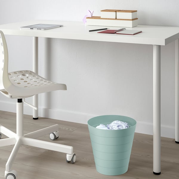 White desk with laptop, books, and green waste bin.