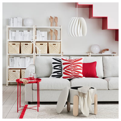 Modern living room with light grey sofa, colourful pillows, red accents, wooden side table, and stylish shelving.