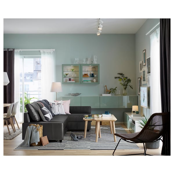 Modern living space with light blue walls, black sofa, striped rug, wooden table, and shelves with decorative items.
