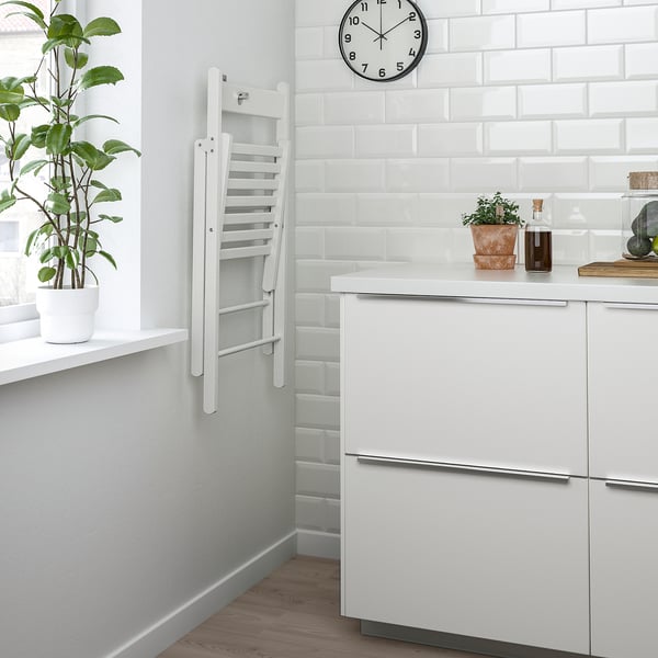 Clean kitchen with hanging white chair. Potted plant, clock, and bottle on counter. White cabinets.