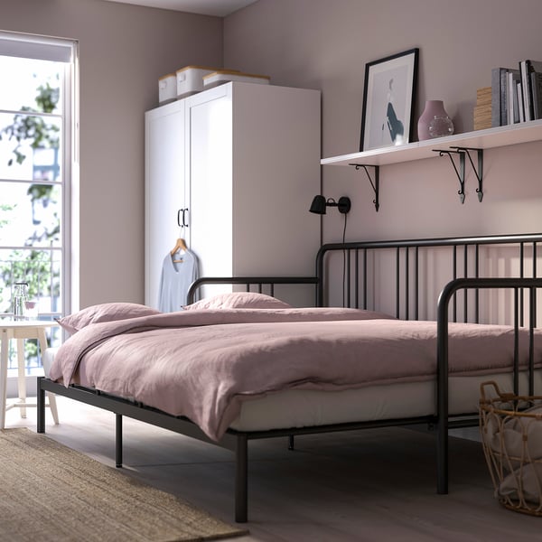Bedroom with FYRESDAL day-bed, closet, and shelves. Day-bed has metal frame and light pink bedding, transforming into a sofa or double bed.