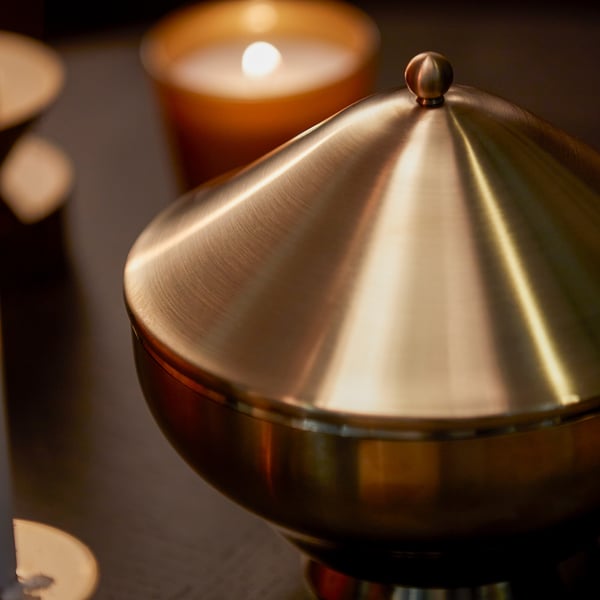 Golden serving bowl with lid, shiny metallic finish, sits on table, reflects light elegantly.