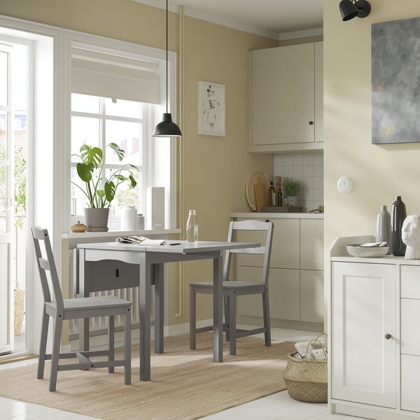 Modern kitchen with beige walls, large window, grey dining set, plant, and art.