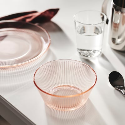 A pink HAVSGÄDDA glass bowl with lines, placed next to a clear glass and a spoon.