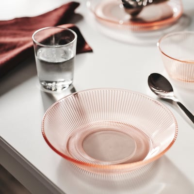 Pink HAVSGÄDDA glass plate with lines, beside water glass and spoon.
