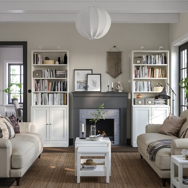 Modern living room with HAVSTA white pine bookcases, beige couches, and a grey fireplace. Decorative lighting and natural decor elements.
