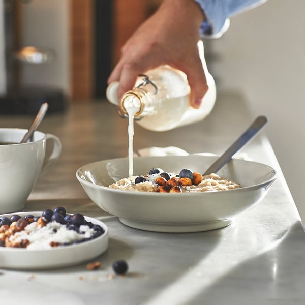 Milk poured on blueberry, hazelnut oatmeal, near coffee and cereal bowls.