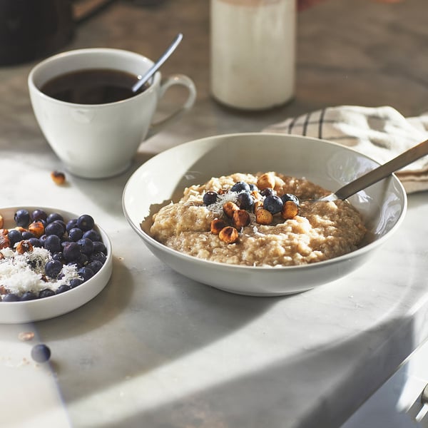 Bowl of oatmeal with blueberries and nuts next to coffee.