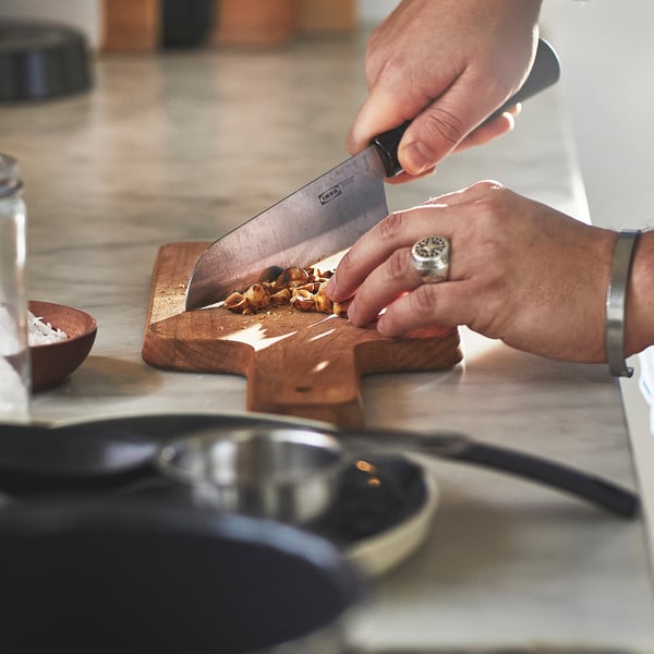 Person chopping food on wooden cutting board using HEMLAGAD knife. Hands visible, wearing watch and ring.