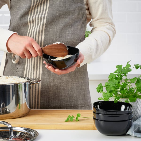 A person is scooping rice with a wooden ladle into a black bowl, demonstrating its non-stick coating and firm grip handle.