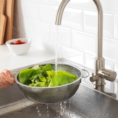 A person washes lettuce in a stainless steel colander under a modern kitchen tap.