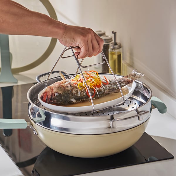 Person lifts steamed fish with clamp, IDEALISK tool. Stainless steel design ensures safe, comfortable grip.