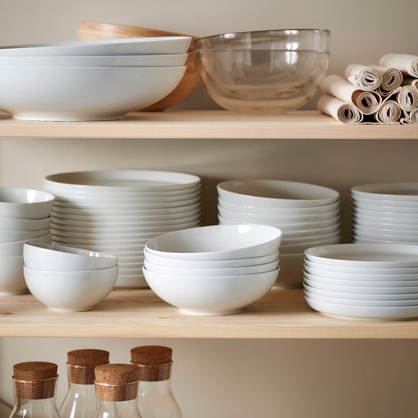 Shelves of white porcelain bowls, plates, and glass containers neatly organised. Includes stacked dinnerware and clear bottles with cork tops.