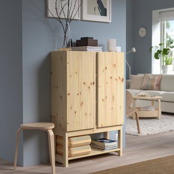 Wooden IVAR cabinet with books & decor against blue wall, stool beside, living room in background.