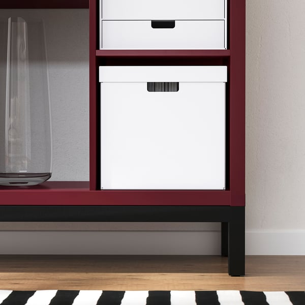 Shelf unit with white boxes and clear vase. Stands sturdy on adjustable feet.