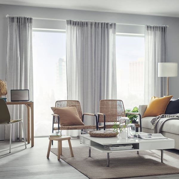 Modern living room with light grey KNARDRUP rug, wicker chairs, white coffee table, and large windows with curtains.