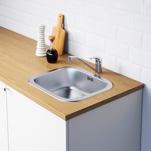 Stainless steel kitchen sink with modern chrome tap, set in wooden countertop with integrated storage and accessories.