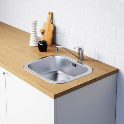 Stainless steel kitchen sink with modern chrome tap, set in wooden countertop with integrated storage and accessories.