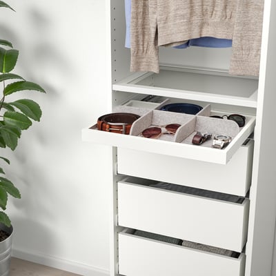 White wardrobe drawer with grey felt trays holding sunglasses, watch, and belt. Plant on left side.