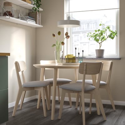 Small, modern dining set with light wood table and grey chairs, situated near a bright window.