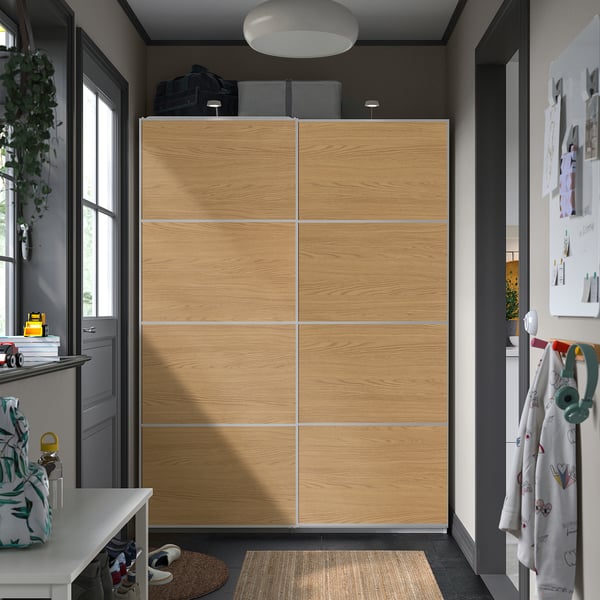 Wooden IKEA MEHAMN wardrobe with light oak sliding doors. Modern, handleless, with table, backpack, rug, and coats.