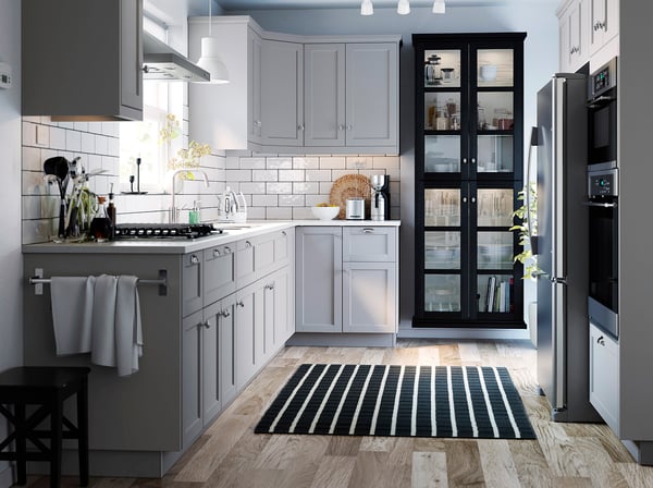 Modern kitchen with grey cabinets, white subway tiles, stainless steel appliances, black and white striped rug, under-cabinet MITTLED lighting.