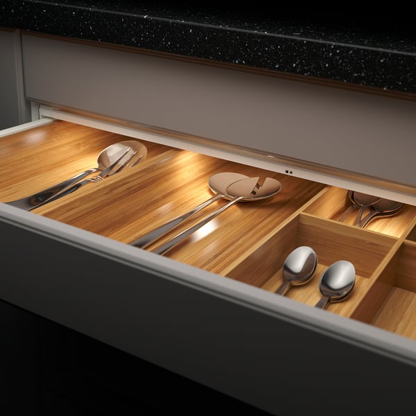 Open drawer reveals wood-lined compartments with organised metallic spoons and ladles. Soft led light illuminates contents.