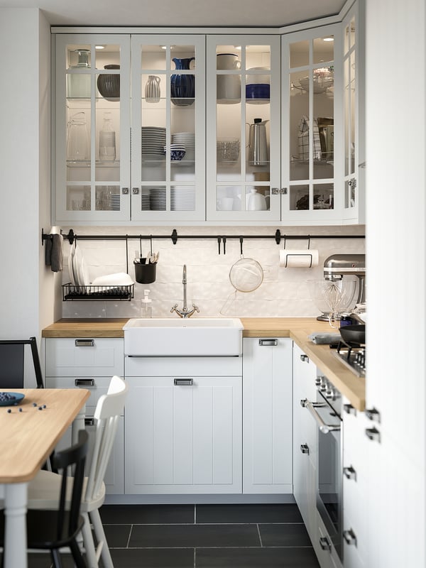 Modern kitchen with white cabinets, glass doors, and built-in led lights, highlighting dinnerware. Wooden countertops and dark floor.