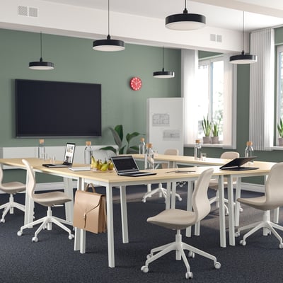 Conference room with MITTZON tables and långfjäll chairs, green walls, modern decor. Light wood tables, beige wheeled chairs, central tv.