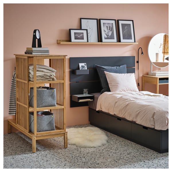 Modern bedroom with peach walls, light wooden shelf, black-framed photos, grey bedding, and fluffy rug.