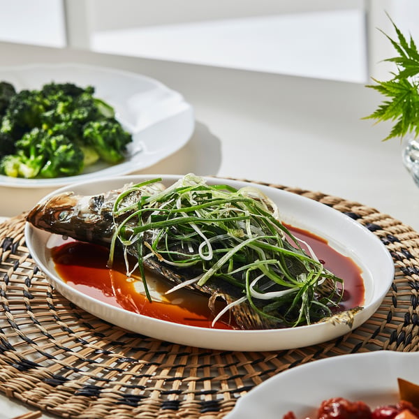 Platter holds cooked fish with green onions atop sauce, flanked by veggie side dishes, reflecting OFTASTs versatile modern serving style.