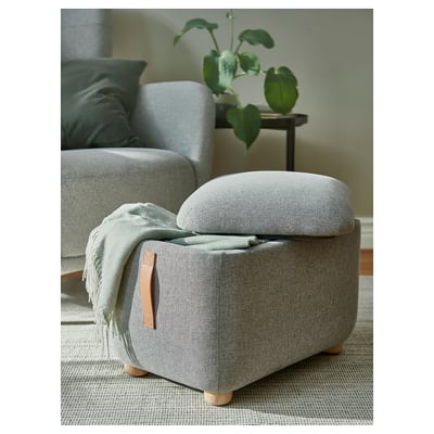 Grey ososhman footstool with leather handle & wooden legs; small, near chair & plant.