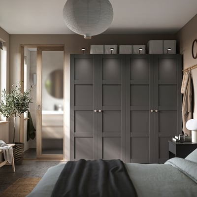 Modern bedroom with dark grey PAX wardrobe, sleek design, natural light, cosy bedding, decorative plants, and a stylish lamp.