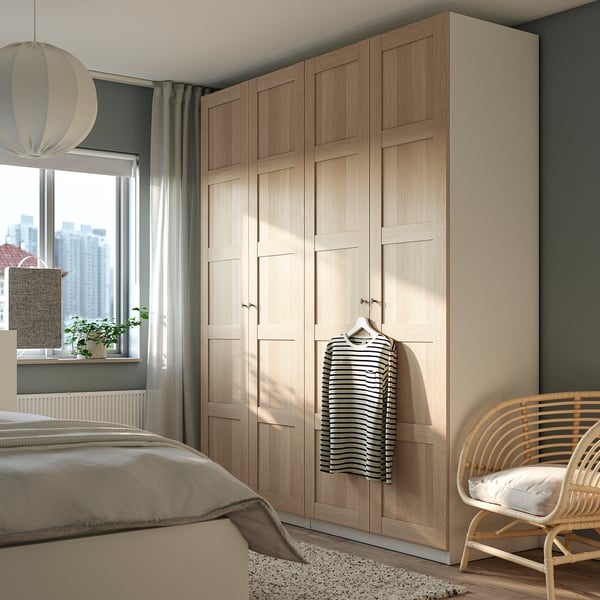 Modern bedroom with grey curtains, white bed, large light wood PAX wardrobe, wicker chair, and striped shirt hanging.