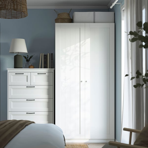 Modern bedroom featuring PAX wardrobe, dresser, and bed. Wardrobe dominates room, holding lamp, books, and decor.