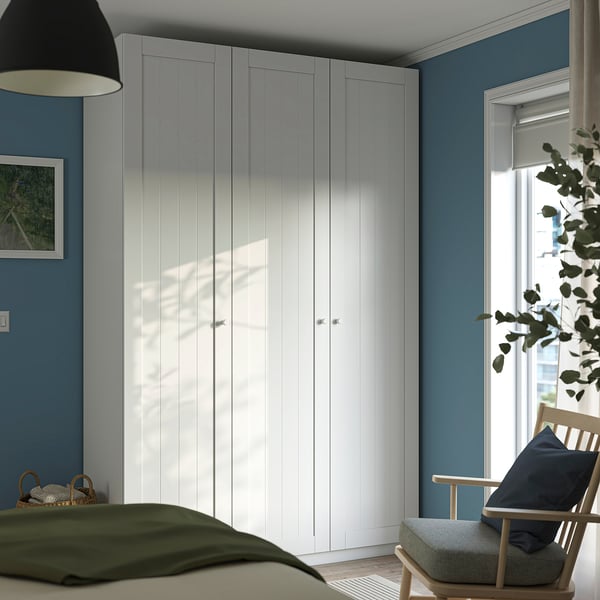 Serene bedroom with PAX wardrobe, wooden chair, and plant by window.